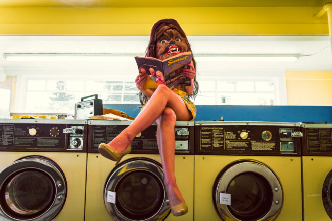 Photograph by Mako Miyamoto. Wookie girl sitting in a yellow vintage laundromat reading a Sunset Magazine